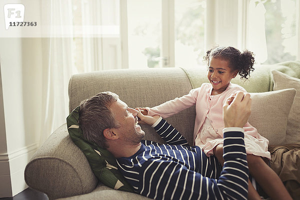 Liebevoller multiethnischer Vater und Tochter  die auf dem Sofa Händchen halten.