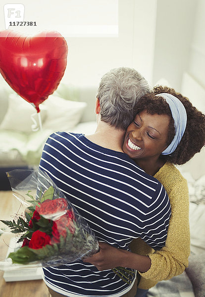 Frau erhält Valentinstag Rosenstrauß und Ballon  umarmender Ehemann