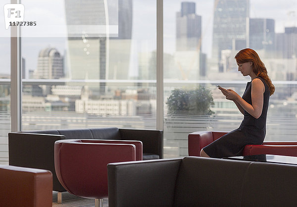 Geschäftsfrau SMS mit Handy in urbaner Lounge mit Stadtansicht
