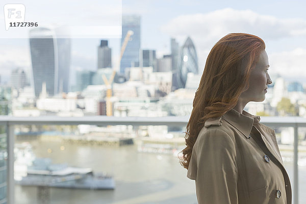 Nachdenkliche Geschäftsfrau mit roten Haaren mit Blick auf die Stadt vom Balkon  London  UK