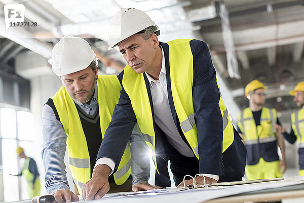Männliche Ingenieure beim Betrachten von Bauplänen auf der Baustelle