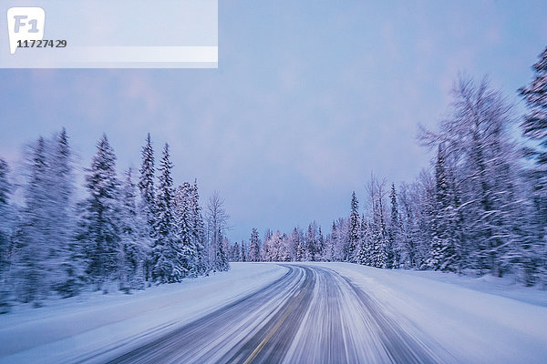 Abgelegene Winterstraße durch schneebedeckte Waldbäume gegen blauen Himmel  Lappland  Finnland