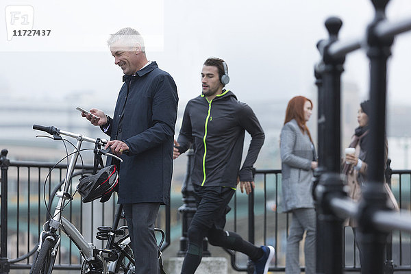 Geschäftsmann mit Fahrrad SMS mit Handy und männlichem Läufer auf urbaner Rampe