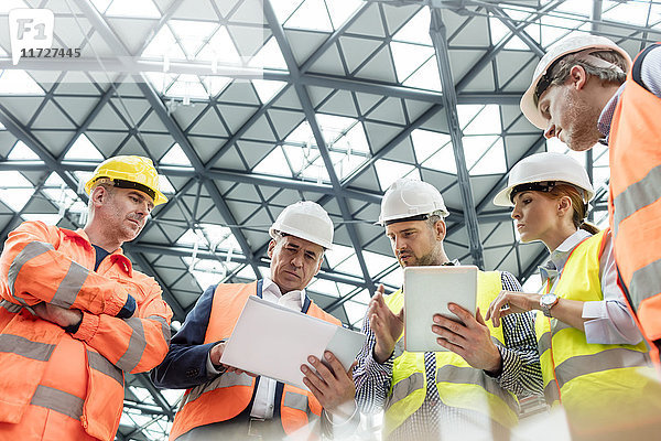Vorarbeiter und Bauarbeiter mit digitalen Tabletts bei der Baustellenbesprechung