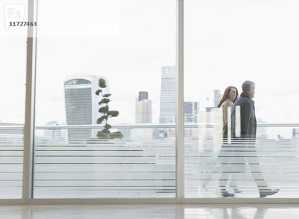 Geschäftsmann und Geschäftsfrau zu Fuß auf dem städtischen Hochhausbalkon mit Blick auf die Stadt