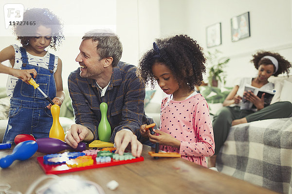 Multi-ethnischer Vater und Töchter beim Spielen mit Spielzeug im Wohnzimmer