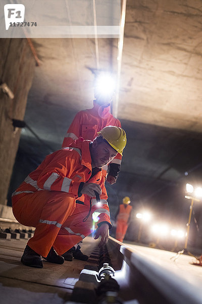 Bauarbeiter untersuchen unterirdische Gleise auf dunkler Baustelle