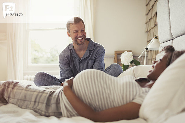 Multi-ethnische schwangere Paare entspannen und lachen auf dem Bett