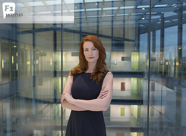 Portrait selbstbewusste Geschäftsfrau mit roten Haaren im modernen Büroatrium