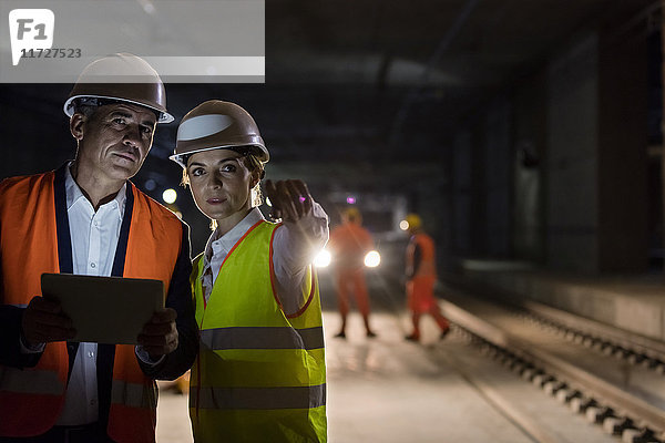 Vorarbeiter und Ingenieur mit digitalem Tablett auf dunklen Gleisen auf der unterirdischen Baustelle