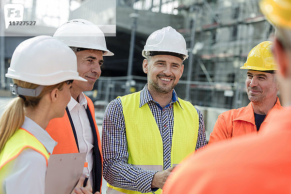 Lächelnde Ingenieure und Bauarbeiter treffen sich auf der Baustelle