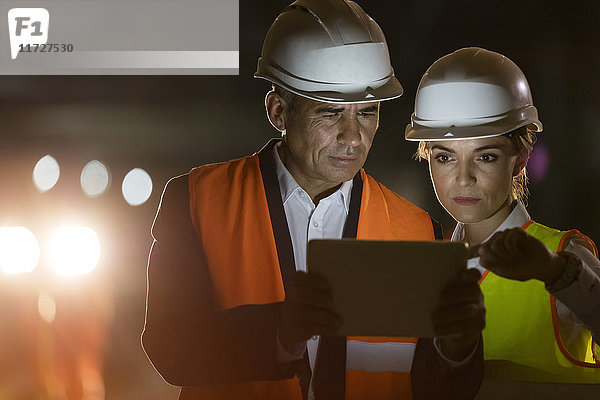 Bauarbeiter und Ingenieur mit digitalem Tablett auf dunkler Baustelle