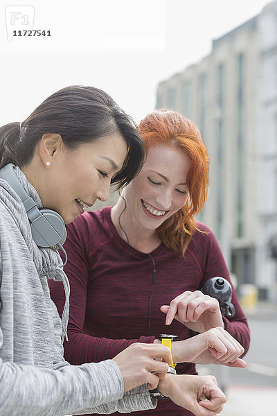 Lächelnde Läuferinnen bei der Suche nach intelligenten Uhren auf dem städtischen Bürgersteig