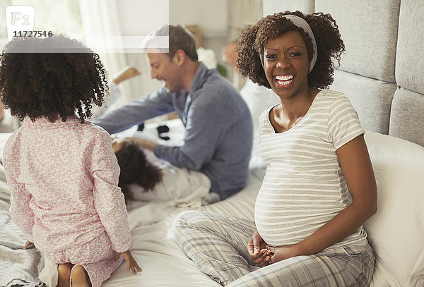 Portrait lachende schwangere Frau mit junger Familie im Bett