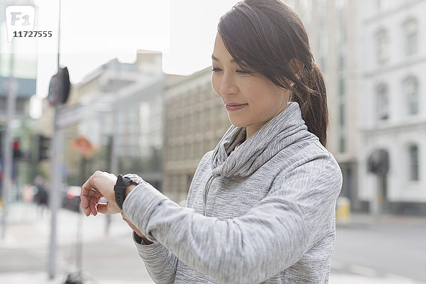 Lächelnde Läuferin prüft Armbanduhr auf städtischem Bürgersteig