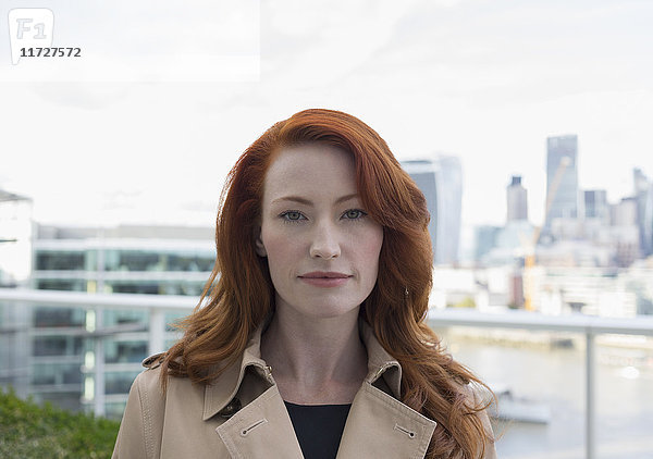 Porträt seriöse  selbstbewusste Geschäftsfrau mit roten Haaren auf Stadtbalkon mit Stadtansicht