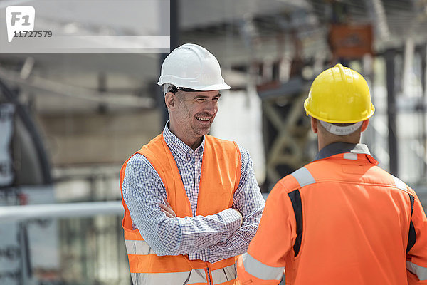 Lächelnder Vorarbeiter im Gespräch mit dem Bauarbeiter auf der Baustelle
