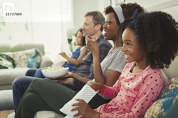 Junge multiethnische Familie schaut Film und isst Popcorn auf dem Sofa.