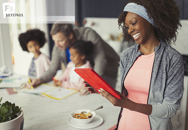 Lächelnde Mutter mit digitalem Tablett und Frühstück in der Küche mit junger Familie