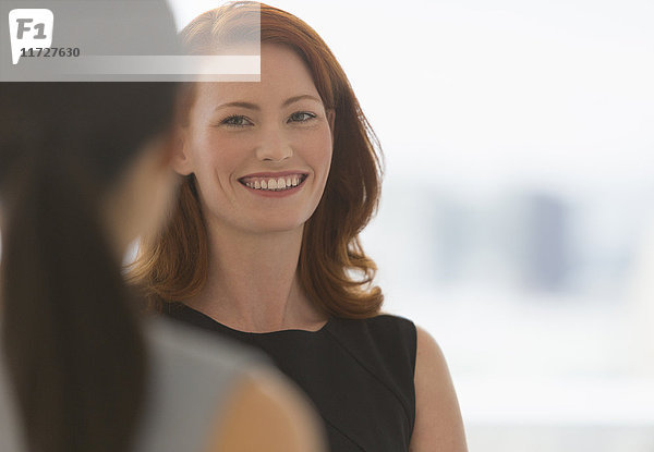 Lächelnde Geschäftsfrau mit roten Haaren im Gespräch mit Kollegen