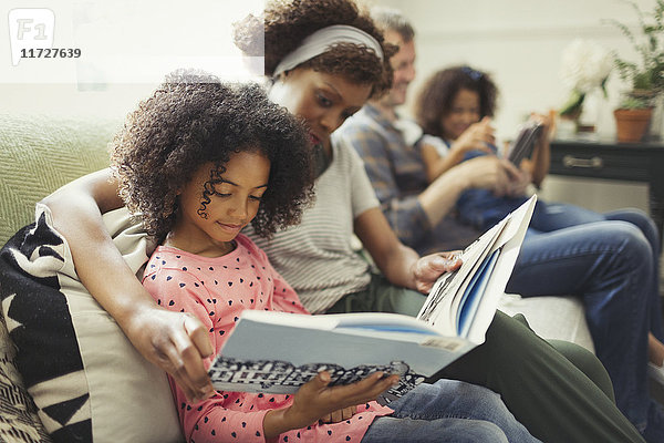 Eltern lesen Bücher mit Töchtern auf dem Wohnzimmersofa