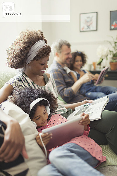 Multi-ethnische junge Familie entspannt sich  liest und benutzt Tablet PCn auf dem Sofa.
