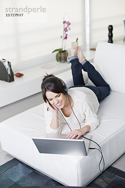 Schöne brünette Frau auf einer Couch mit Computer und Kopfhörer