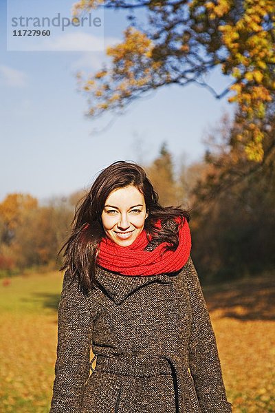 Porträt einer brünetten Frau im Park im Herbst lächelnd vor der Kamera