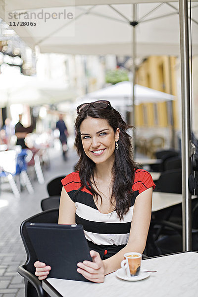 Porträt einer Frau mit Tablette bei einem Kaffee im Freien mit Blick auf die Kamera