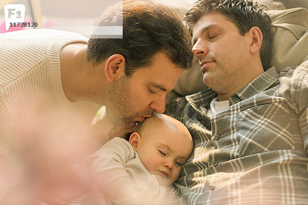 Zärtliche männliche schwule Eltern küssen schlafenden Baby-Sohn