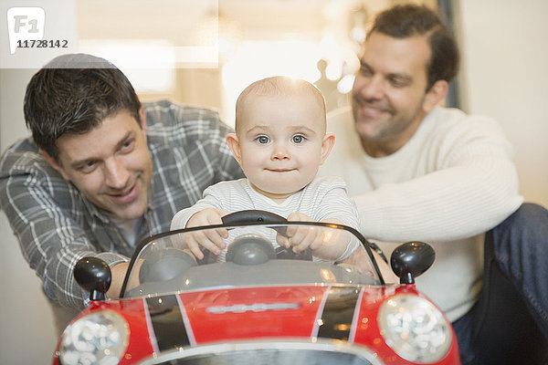 Portrait männliche schwule Eltern schieben Baby Sohn in Spielzeugauto
