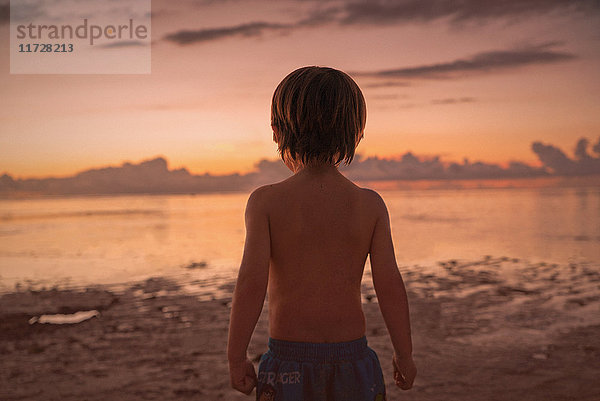 Junge am Strand mit Blick auf ruhigen Sonnenuntergang Meer