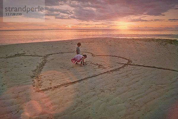 Junge und Mädchen Bruder und Schwester Zeichnung Herz-Form in Sand auf ruhigen Sonnenuntergang Strand