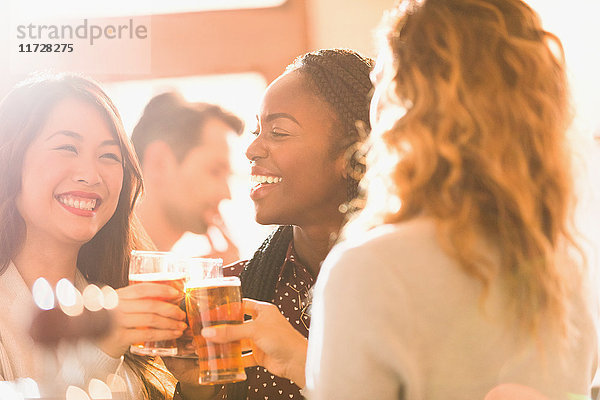 Lächelnde Freundinnen stoßen mit Biergläsern in einer Bar an