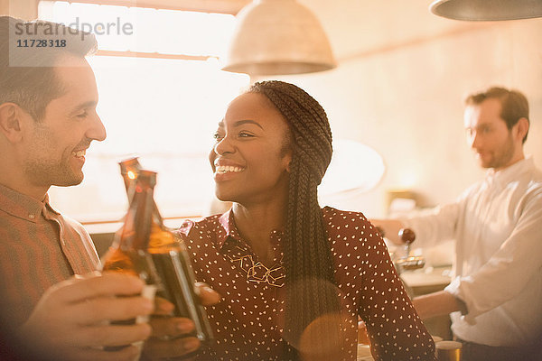 Lächelndes Paar  das in einer Bar mit Bierflaschen anstößt