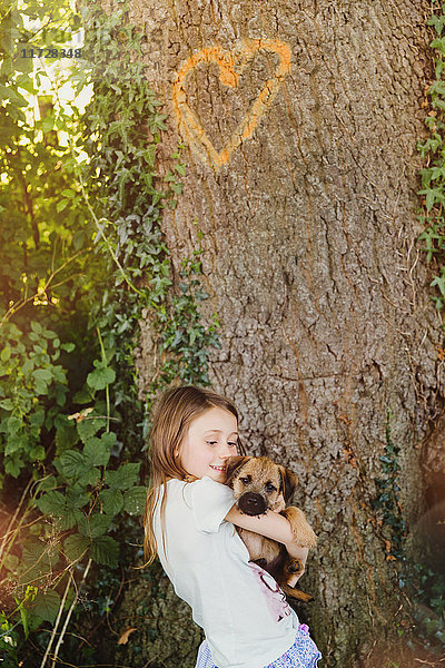 Mädchen hält Hundewelpe unter Baum mit Herzform
