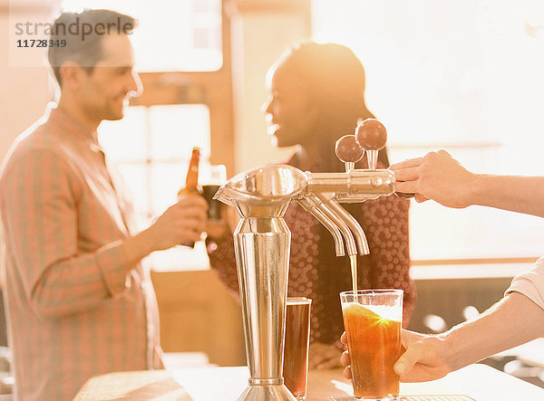 Paar trinkt Bier hinter einem Barkeeper  der Bier am Zapfhahn in einer Bar ausschenkt