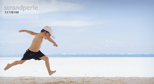 Verspielter Junge läuft am tropischen Strand