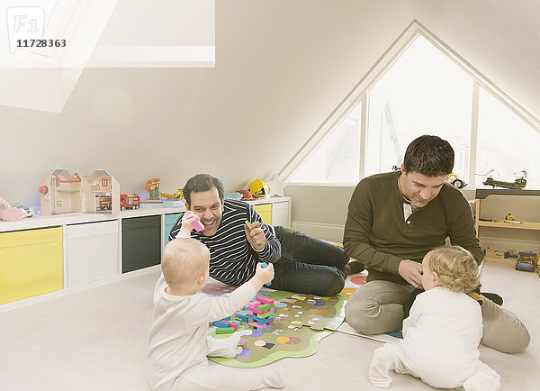 Männliche schwule Eltern spielen mit Babysöhnen im Spielzimmer