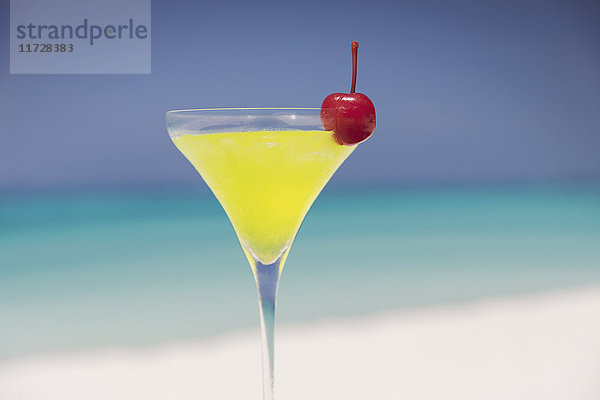 Close up gelben Cocktail mit Kirsche in Martini Glas auf sonnigen tropischen Strand