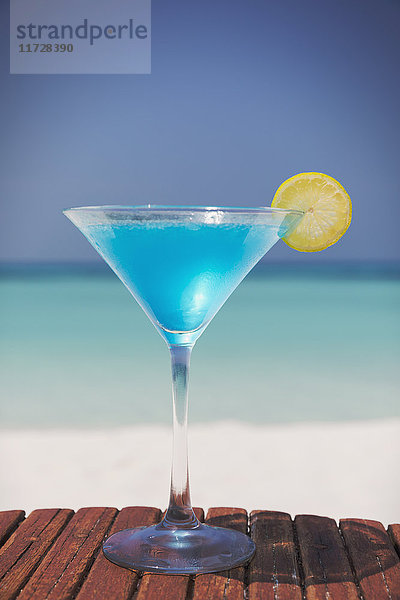 Blauer Cocktail mit Zitronenscheibe im Martiniglas am sonnigen tropischen Strand