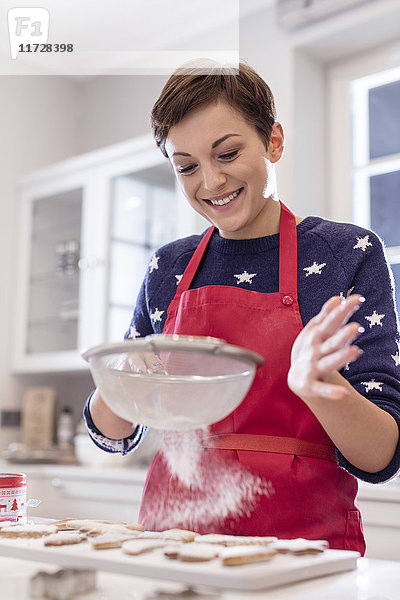 Lächelnde Frau beim Backen  Sieben von Zucker über Kekse in der Küche