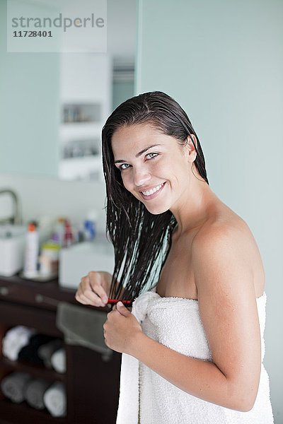 Brünette Frau bürstet sich die Haare und lächelt in die Kamera.