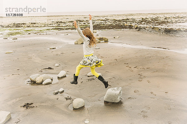 Übermütiges Mädchen springt vor Freude auf Strandfelsen
