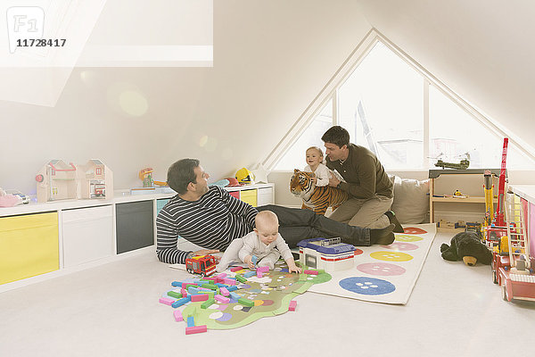 Männliche schwule Eltern spielen mit Babysöhnen im Spielzimmer