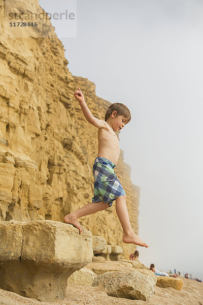 Junge in Badehose springt auf Strandfelsen