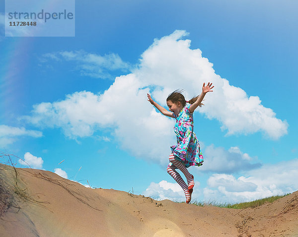 Überschwängliches Mädchen springt vor Freude am Strand Hügel unter sonnigen blauen Himmel mit Wolken