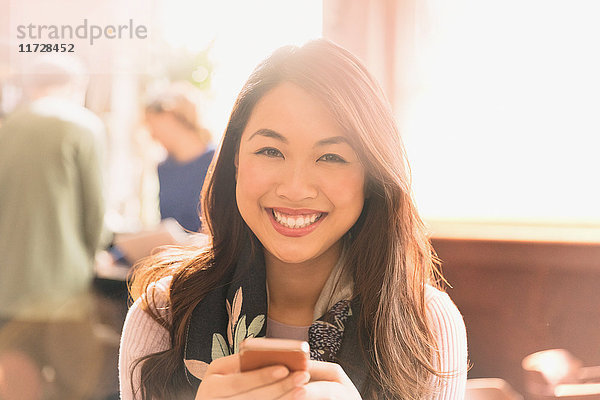 Porträt einer lächelnden chinesischen Frau  die in einem Café eine SMS mit ihrem Handy schreibt