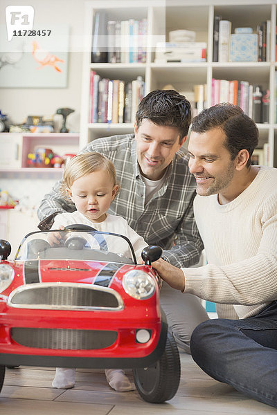Männliche schwule Eltern schieben Baby Sohn in Spielzeugauto
