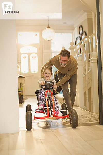 Vater schiebt Tochter auf Spielzeugauto im Foyerflur